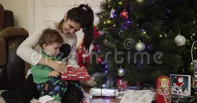美丽的年轻母亲和儿子微笑着在圣诞树附近打开礼物。 2016年圣诞节。 4K. 高清高清